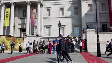 Visitors-queue-at-the-National-Portrait-Gallery-in-sunny-Trafalgar-Square,-London,-showcasing-urban-life-and-tourism