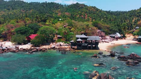 Aerial-drone-shot-of-a-tropical-beach-resort-surrounded-by-lush-greenery-and-crystal-clear-waters,-showcasing-a-serene-coastal-landscape-in-Thailand