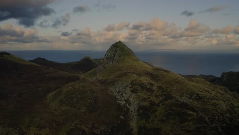 Slow-aerial-looking-over-rocky-peak-in-the-Scottish-Highlands-and-the-sea-on-the-horizon,-Isle-of-Skye,-Scotland