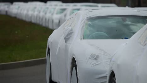 New-cars-covered-in-protective-sheets-lined-up-in-an-outdoor-lot