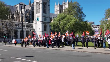 Protesters-with-flags-march-for-workers'-rights-at-Parliament-Square-Garden,-sunny-day,-vibrant-scene