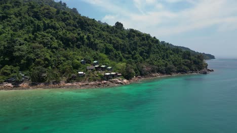 Island-Hill-Huts-in-lush-Jungle-fores,-emerald-waters-lagoon