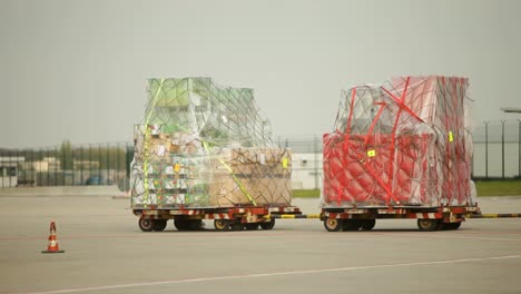 Two-cargo-pallets-wrapped-in-nets-on-tarmac,-ready-for-air-transport,-clear-daylight,-no-people