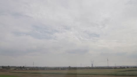 Countryside-landscape-seen-from-a-moving-train,-capturing-fields-and-a-cloudy-sky