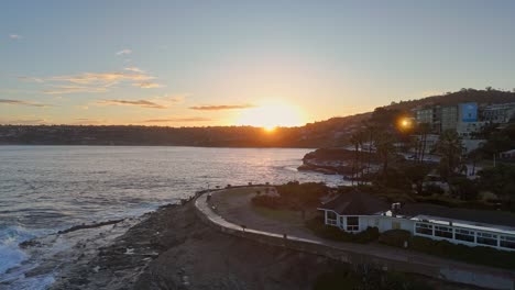 La-Jolla-Cove-Drohne-Fliegt-In-Richtung-Sonnenaufgang-über-Den-Wellen-Der-Parkhalbinsel,-Vögel-Und-Seelöwen-Sorgen-Für-Bewegung