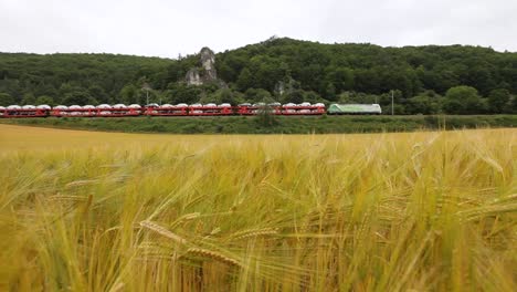 Freight-train-loaded-with-cars-passing-by-lush-green-fields,-showcasing-vibrant-rural-transport-scene