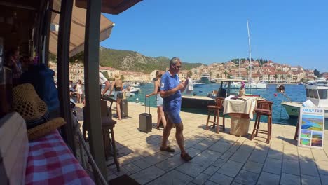 Tourist-People-Walking-with-Luggage-Suitcases-on-Promenade-of-Hvar-island-in-Croatia,-Static-Shot