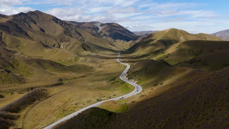 A-winding-road-through-the-lindis-pass-in-new-zealand,-showcasing-rugged-terrain-and-remote-beauty,-aerial-view