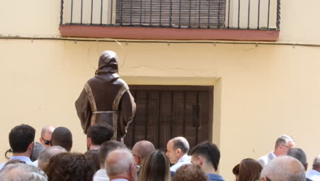 A-statue-brown-religious-attire-stands-facing-a-crowd-during-a-Spanish-communion