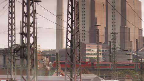 Urban-train-passing-through-industrial-area-with-modern-buildings-in-the-background,-overcast-sky