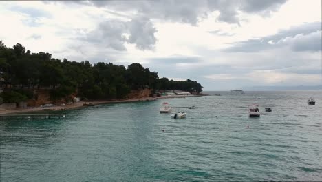 Croatian-landscape-by-the-sea,-small-boats,-yacht-in-distance,-drone-shot-low-to-a-few-meters