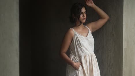 Young-woman-in-white-dress-standing-pensively-in-a-dimly-lit-concrete-hallway