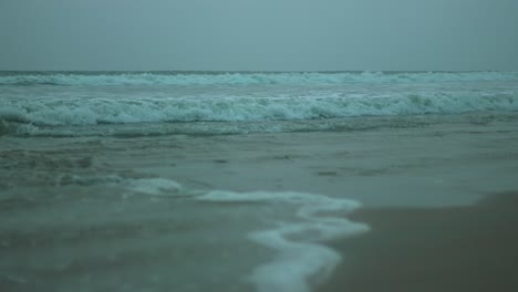 Moody-waves-crashing-on-a-sandy-beach-under-overcast-skies,-calm-yet-powerful
