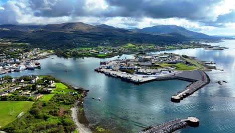 Drohnenaufnahme-Des-Fischereihafens-Von-Castletownbere-Mit-Im-Geschützten-Hafen-Angedockten-Fischtrawlern-Und-Im-Hintergrund-Das-Fischerdorf-Und-Das-Touristenresort-Mit-Den-Bergen-Rund-Um-Den-Hafen