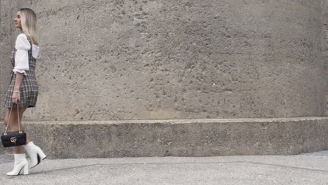 Wide-shot-of-blonde-women-walking-past-wall-in-slow-motion-holding-a-Gucci-bag