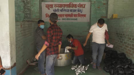 Eine-Weitwinkelaufnahme-Indischer-Bürger-Einer-Ländlichen-Stadt-In-Bihar,-Die-Während-Der-Coronavirus-Ausgangssperre-Lebensmittelpakete-Für-Migranten,-Tagelöhner-Und-Obdachlose-Vorbereiten