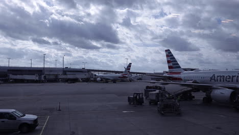 View-of-airplanes-at-airport-gate-and-small-truck-and-cargo-drive-by-on-cloudy-grey-day,-static