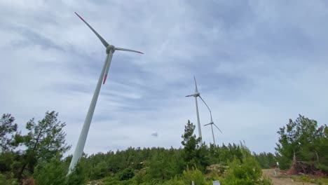 Ultra-wide-angle-view-of-wind-power-turbines-with-propellers-fast-spinning-against-windy-overcast-sky,-Datça-peninsula,-Aegean-Turkey