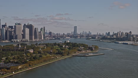 NYC-New-York-Aerial-v188-low-flyover-Buttermilk-Channel-capturing-Governors-Island,-cityscape-of-Brooklyn-and-Manhattan-with-helicopter-flying-across-the-sky---Shot-with-Inspire-3-8k---September-2023