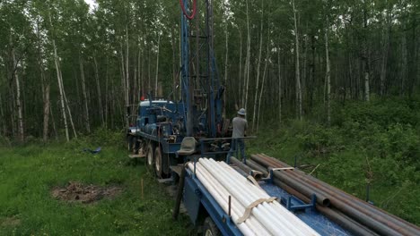 Zoom-in-aerial-view-of-water-well-drilling-operator-removing-lengths-of-drill-pipe-from-boring-hole