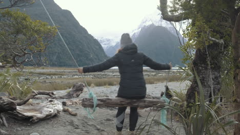 Girl-alone-swinging-on-wooden-swing-with-incredible-view-of-snow-capped-mountains-and-fiords-in-the-background