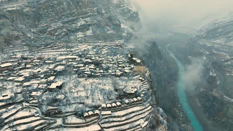 Luftaufnahme-Des-Schneebedeckten-Karimabad-Auf-Einer-Klippe-Neben-Dem-Fluss