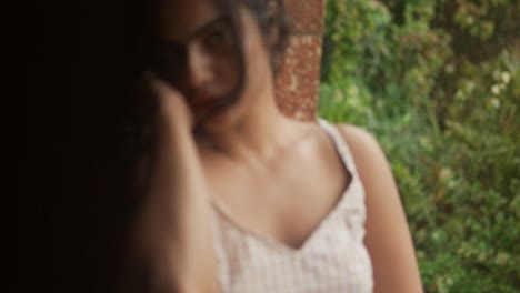 Mujer-Joven-Con-Gafas-De-Sol-Sentada-Junto-Al-Río-De-La-Ciudad-Durante-El-Día-Soleado,-Puente-En-El-Fondo,-Primer-Plano