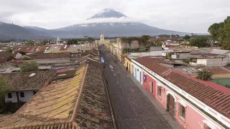 Toma-Aérea-De-La-Calle-Que-Conduce-Al-Arco-De-Santa-Catalina-Con-El-Volcán-De-Agua-Al-Fondo.