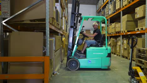 Man-in-a-forklift-moving-pallet-on-shelf-in-large-warehouse