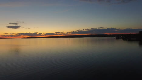 Ein-Boot-Fährt-über-Einen-Ruhigen-See,-Während-Der-Sonnenuntergang-Einen-Orangefarbenen-Schimmer-Am-Horizont-Hinterlässt