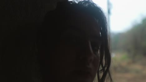 Woman-peeking-from-a-dark-corner-with-a-somber-expression,-slightly-blurred-foreground