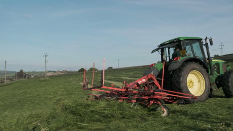 Granjero-Que-Conduce-Un-Gran-Tractor-Verde-Que-Remolca-Una-Cortadora-De-Césped-Que-Agita-Y-Escupe-Masas-De-Hierba-Mientras-Pasa