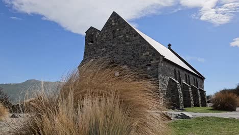 Charming-stone-anglican-church-on-the-shore-of-Lake-Tekapo-surrounded-by-mountains-and-matagouri-bushes-moved-softly-by-the-wind