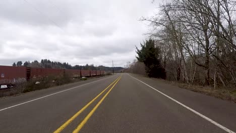 Fahren-Sie-Die-Straße-Entlang-Neben-Einem-Mit-Graffiti-Bedeckten-Zug,-Der-Neben-Einem-Fluss-In-Oregon-Steht