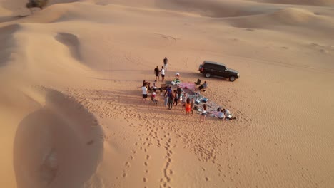 Aerial-view-from-drone-of-multinational-friends-preparing-barbecue-in-the-desert-in-Abu-Dhabi,-United-Arab-Emirates