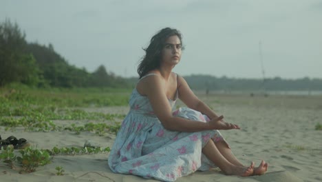 Young-woman-sitting-thoughtfully-on-a-tropical-beach-at-dusk,-gentle-waves-in-the-background