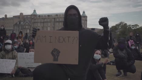 Black-man-with-mask-in-black-clothes-lifting-his-fist-and-holding-a-banner-during-black-lives-matter-protest