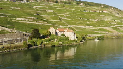 Aerial-shot-passing-in-front-of-castle-along-the-shore-of-Lake-Léman-in-Lavaux-vineyard,-Switzerland-Swiss-train-passing-just-behind-the-castle-Chateau-de-Glérolles,-Lavaux---Switzerland