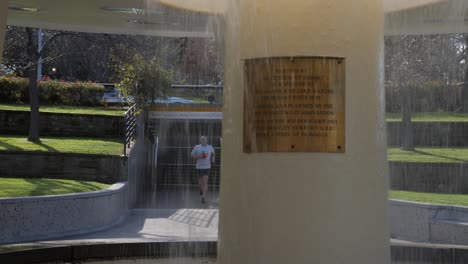 Male-runner-stops-to-check-watch-behind-ABC-roundabout-waterfountain-in-Hobart,-Tasmania,-Australia