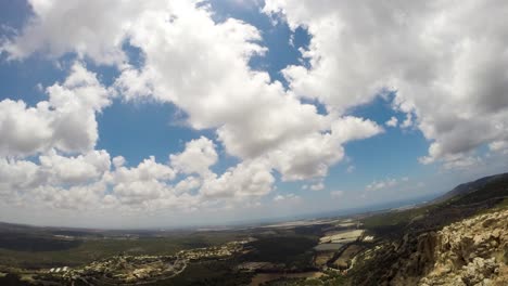 Ein-Zeitraffer-Von-Wolken,-Die-In-Der-Nähe-Einer-Klippe-über-Einem-Dorf-Vorbeiziehen.-Die-Wolken-Ziehen-Langsam-Und-Vorsichtig-Vorbei-Und-Manchmal-Kann-Man-Einen-Typen-Sehen,-Der-In-Der-Nähe-Der-Klippe-Spaß-Hat.