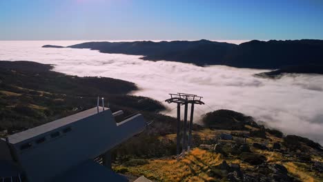 Aerial-fly-over-ski-chairlift-cable-to-reveal-morning-fog-above-the-mountain-forest-at-Thredbo,-NSW,-Australia