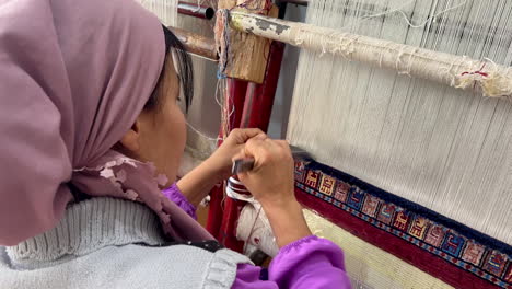 Hands-of-a-woman-are-weaving-carpet-tools-and-threads-handmade-in-Uzbekistan-Samarkand-Bukhara-carpet,-textile-production-folk-traditional-Muslim-work-copy-space