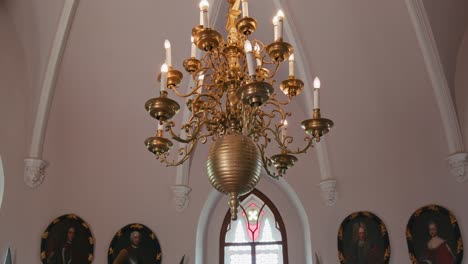 Elegant-golden-chandelier-with-intricate-designs,-lighting-up-Trakoscan-Castle's-Chivalric-Hall,-framed-by-arched-windows-and-historical-portraits