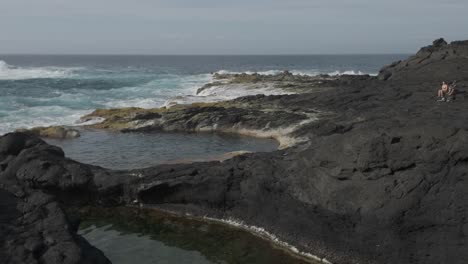 Natural-pools-on-volcanic-rocks-with-people-relaxing,-Mosteiros,-Sao-Miguel,-wide-shot