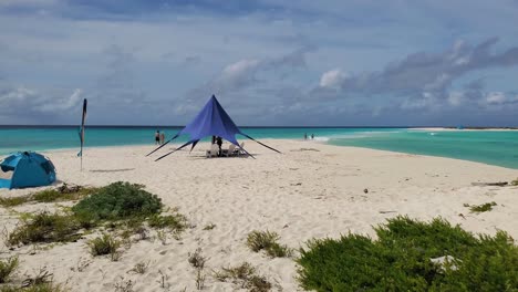 Lonely-beach-with-few-people-walking-towards-isthmus-of-cayo-de-agua,-waves-breaking-background,-pan-right