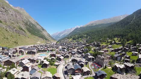 Vuelo-Sobre-Zermatt-Con-Vistas-Al-Tranquilo-Y-Pacífico-Pueblo-Alpino-Lleno-De-Cabañas-Tradicionales-Durante-El-Hermoso-Día-De-Primavera-En-Los-Alpes-Suizos,-Suiza,-Europa.