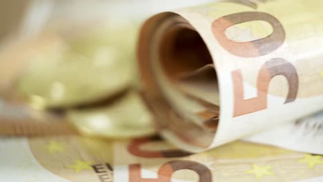 Primer-Plano-De-Billetes-De-50-Euros-Y-Monedas-De-Oro-Que-Giran-La-Exhibición-De-Dinero