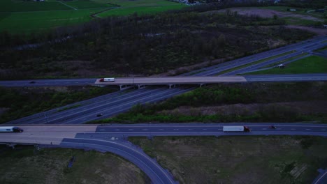 Vista-Aérea-Del-Cruce-De-Autopistas-Con-Semirremolques-Circulando-Al-Atardecer.