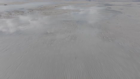 Low-aerial-pan-up-and-reveal-of-mountains-bordering-the-Great-Salt-Lake,-Utah-on-a-sunny-spring-day