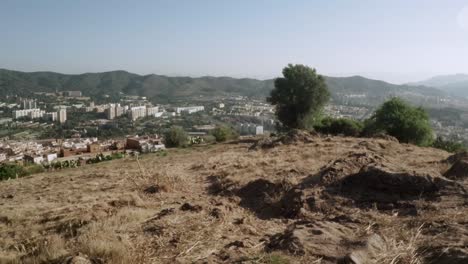 Cámara-Aérea-De-Drones-Retrocediendo-Disfrutando-De-Una-Vista-De-La-Ciudad-En-La-Cima-De-Una-Montaña-En-Un-Día-Soleado